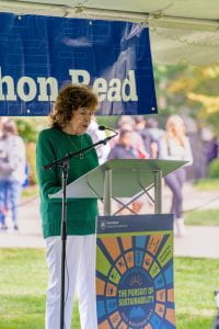 Susan Paterno reads from podium under white tent